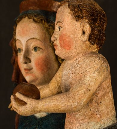 Zdjęcie nr 17: Rzeźba drążona, ukazująca Matkę Boską z Dzieciątkiem. Maria ustawiona frontalnie, w delikatnym kontrapoście, na lewym ręku trzyma Dzieciątko, w prawym dzierży berło. Twarz okrągła z wysokim czołem, drobnymi ustami i małymi oczami o delikatnie zarysowanych łukach brwiowych. Włosy jasne, ułożone w skręcone pukle spływające na plecy. Maria ubrana jest w białą suknię zdobioną drobnymi, niebieskimi gwiazdkami, ciemnobłękitny płaszcz z bordową podszewką spięty na piersi oraz spiczaste, brązowe buty. Na głowie ma założony ciemnoniebieski welon z bordową podszewką, spływający na ramiona i piersi oraz brązową podstawę do niezachowanej korony. Draperia szat miękka o wyraźnie zaznaczonych, licznych fałdach misowych i kaskadowych. Dzieciątko ukazane w pozycji siedzącej, zwrócone w prawo. W lewej dłoni trzyma jabłko królewskie, a prawą wyprostowaną podnosi na wysokość tułowia. Twarz pełna o dziecięcych rysach z małymi ustami, okolona krótkimi i kędzierzawymi włosami. Polichromia w odsłoniętych partiach ciała naturalistyczna, berło polichromowane na brązowo.