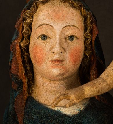 Zdjęcie nr 14: Rzeźba drążona, ukazująca Matkę Boską z Dzieciątkiem. Maria ustawiona frontalnie, w delikatnym kontrapoście, na lewym ręku trzyma Dzieciątko, w prawym dzierży berło. Twarz okrągła z wysokim czołem, drobnymi ustami i małymi oczami o delikatnie zarysowanych łukach brwiowych. Włosy jasne, ułożone w skręcone pukle spływające na plecy. Maria ubrana jest w białą suknię zdobioną drobnymi, niebieskimi gwiazdkami, ciemnobłękitny płaszcz z bordową podszewką spięty na piersi oraz spiczaste, brązowe buty. Na głowie ma założony ciemnoniebieski welon z bordową podszewką, spływający na ramiona i piersi oraz brązową podstawę do niezachowanej korony. Draperia szat miękka o wyraźnie zaznaczonych, licznych fałdach misowych i kaskadowych. Dzieciątko ukazane w pozycji siedzącej, zwrócone w prawo. W lewej dłoni trzyma jabłko królewskie, a prawą wyprostowaną podnosi na wysokość tułowia. Twarz pełna o dziecięcych rysach z małymi ustami, okolona krótkimi i kędzierzawymi włosami. Polichromia w odsłoniętych partiach ciała naturalistyczna, berło polichromowane na brązowo.