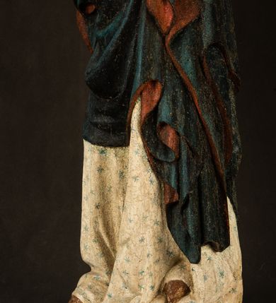 Zdjęcie nr 23: Rzeźba drążona, ukazująca Matkę Boską z Dzieciątkiem. Maria ustawiona frontalnie, w delikatnym kontrapoście, na lewym ręku trzyma Dzieciątko, w prawym dzierży berło. Twarz okrągła z wysokim czołem, drobnymi ustami i małymi oczami o delikatnie zarysowanych łukach brwiowych. Włosy jasne, ułożone w skręcone pukle spływające na plecy. Maria ubrana jest w białą suknię zdobioną drobnymi, niebieskimi gwiazdkami, ciemnobłękitny płaszcz z bordową podszewką spięty na piersi oraz spiczaste, brązowe buty. Na głowie ma założony ciemnoniebieski welon z bordową podszewką, spływający na ramiona i piersi oraz brązową podstawę do niezachowanej korony. Draperia szat miękka o wyraźnie zaznaczonych, licznych fałdach misowych i kaskadowych. Dzieciątko ukazane w pozycji siedzącej, zwrócone w prawo. W lewej dłoni trzyma jabłko królewskie, a prawą wyprostowaną podnosi na wysokość tułowia. Twarz pełna o dziecięcych rysach z małymi ustami, okolona krótkimi i kędzierzawymi włosami. Polichromia w odsłoniętych partiach ciała naturalistyczna, berło polichromowane na brązowo.