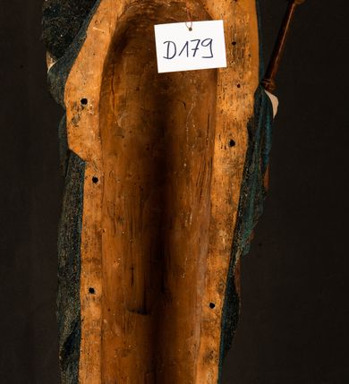 Zdjęcie nr 22: Rzeźba drążona, ukazująca Matkę Boską z Dzieciątkiem. Maria ustawiona frontalnie, w delikatnym kontrapoście, na lewym ręku trzyma Dzieciątko, w prawym dzierży berło. Twarz okrągła z wysokim czołem, drobnymi ustami i małymi oczami o delikatnie zarysowanych łukach brwiowych. Włosy jasne, ułożone w skręcone pukle spływające na plecy. Maria ubrana jest w białą suknię zdobioną drobnymi, niebieskimi gwiazdkami, ciemnobłękitny płaszcz z bordową podszewką spięty na piersi oraz spiczaste, brązowe buty. Na głowie ma założony ciemnoniebieski welon z bordową podszewką, spływający na ramiona i piersi oraz brązową podstawę do niezachowanej korony. Draperia szat miękka o wyraźnie zaznaczonych, licznych fałdach misowych i kaskadowych. Dzieciątko ukazane w pozycji siedzącej, zwrócone w prawo. W lewej dłoni trzyma jabłko królewskie, a prawą wyprostowaną podnosi na wysokość tułowia. Twarz pełna o dziecięcych rysach z małymi ustami, okolona krótkimi i kędzierzawymi włosami. Polichromia w odsłoniętych partiach ciała naturalistyczna, berło polichromowane na brązowo.