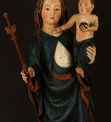 Zdjęcie nr 5: Rzeźba drążona, ukazująca Matkę Boską z Dzieciątkiem. Maria ustawiona frontalnie, w delikatnym kontrapoście, na lewym ręku trzyma Dzieciątko, w prawym dzierży berło. Twarz okrągła z wysokim czołem, drobnymi ustami i małymi oczami o delikatnie zarysowanych łukach brwiowych. Włosy jasne, ułożone w skręcone pukle spływające na plecy. Maria ubrana jest w białą suknię zdobioną drobnymi, niebieskimi gwiazdkami, ciemnobłękitny płaszcz z bordową podszewką spięty na piersi oraz spiczaste, brązowe buty. Na głowie ma założony ciemnoniebieski welon z bordową podszewką, spływający na ramiona i piersi oraz brązową podstawę do niezachowanej korony. Draperia szat miękka o wyraźnie zaznaczonych, licznych fałdach misowych i kaskadowych. Dzieciątko ukazane w pozycji siedzącej, zwrócone w prawo. W lewej dłoni trzyma jabłko królewskie, a prawą wyprostowaną podnosi na wysokość tułowia. Twarz pełna o dziecięcych rysach z małymi ustami, okolona krótkimi i kędzierzawymi włosami. Polichromia w odsłoniętych partiach ciała naturalistyczna, berło polichromowane na brązowo.