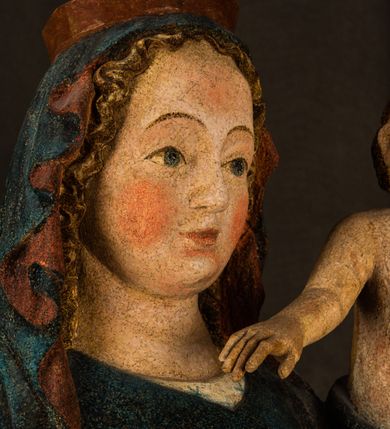 Zdjęcie nr 12: Rzeźba drążona, ukazująca Matkę Boską z Dzieciątkiem. Maria ustawiona frontalnie, w delikatnym kontrapoście, na lewym ręku trzyma Dzieciątko, w prawym dzierży berło. Twarz okrągła z wysokim czołem, drobnymi ustami i małymi oczami o delikatnie zarysowanych łukach brwiowych. Włosy jasne, ułożone w skręcone pukle spływające na plecy. Maria ubrana jest w białą suknię zdobioną drobnymi, niebieskimi gwiazdkami, ciemnobłękitny płaszcz z bordową podszewką spięty na piersi oraz spiczaste, brązowe buty. Na głowie ma założony ciemnoniebieski welon z bordową podszewką, spływający na ramiona i piersi oraz brązową podstawę do niezachowanej korony. Draperia szat miękka o wyraźnie zaznaczonych, licznych fałdach misowych i kaskadowych. Dzieciątko ukazane w pozycji siedzącej, zwrócone w prawo. W lewej dłoni trzyma jabłko królewskie, a prawą wyprostowaną podnosi na wysokość tułowia. Twarz pełna o dziecięcych rysach z małymi ustami, okolona krótkimi i kędzierzawymi włosami. Polichromia w odsłoniętych partiach ciała naturalistyczna, berło polichromowane na brązowo.