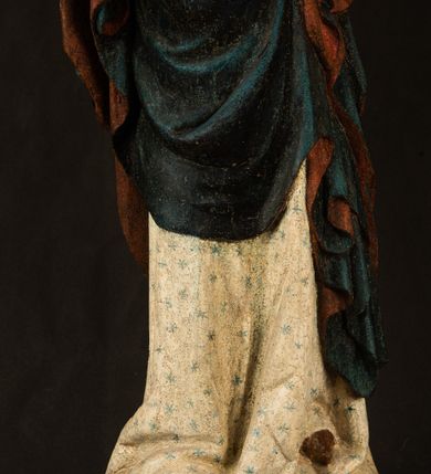 Zdjęcie nr 3: Rzeźba drążona, ukazująca Matkę Boską z Dzieciątkiem. Maria ustawiona frontalnie, w delikatnym kontrapoście, na lewym ręku trzyma Dzieciątko, w prawym dzierży berło. Twarz okrągła z wysokim czołem, drobnymi ustami i małymi oczami o delikatnie zarysowanych łukach brwiowych. Włosy jasne, ułożone w skręcone pukle spływające na plecy. Maria ubrana jest w białą suknię zdobioną drobnymi, niebieskimi gwiazdkami, ciemnobłękitny płaszcz z bordową podszewką spięty na piersi oraz spiczaste, brązowe buty. Na głowie ma założony ciemnoniebieski welon z bordową podszewką, spływający na ramiona i piersi oraz brązową podstawę do niezachowanej korony. Draperia szat miękka o wyraźnie zaznaczonych, licznych fałdach misowych i kaskadowych. Dzieciątko ukazane w pozycji siedzącej, zwrócone w prawo. W lewej dłoni trzyma jabłko królewskie, a prawą wyprostowaną podnosi na wysokość tułowia. Twarz pełna o dziecięcych rysach z małymi ustami, okolona krótkimi i kędzierzawymi włosami. Polichromia w odsłoniętych partiach ciała naturalistyczna, berło polichromowane na brązowo.