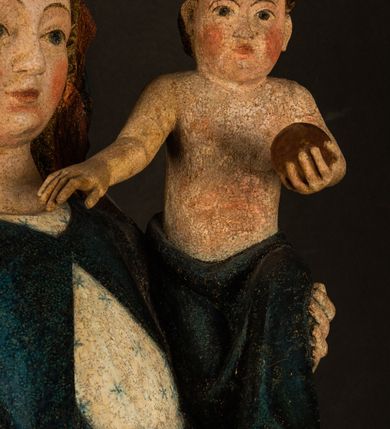 Zdjęcie nr 7: Rzeźba drążona, ukazująca Matkę Boską z Dzieciątkiem. Maria ustawiona frontalnie, w delikatnym kontrapoście, na lewym ręku trzyma Dzieciątko, w prawym dzierży berło. Twarz okrągła z wysokim czołem, drobnymi ustami i małymi oczami o delikatnie zarysowanych łukach brwiowych. Włosy jasne, ułożone w skręcone pukle spływające na plecy. Maria ubrana jest w białą suknię zdobioną drobnymi, niebieskimi gwiazdkami, ciemnobłękitny płaszcz z bordową podszewką spięty na piersi oraz spiczaste, brązowe buty. Na głowie ma założony ciemnoniebieski welon z bordową podszewką, spływający na ramiona i piersi oraz brązową podstawę do niezachowanej korony. Draperia szat miękka o wyraźnie zaznaczonych, licznych fałdach misowych i kaskadowych. Dzieciątko ukazane w pozycji siedzącej, zwrócone w prawo. W lewej dłoni trzyma jabłko królewskie, a prawą wyprostowaną podnosi na wysokość tułowia. Twarz pełna o dziecięcych rysach z małymi ustami, okolona krótkimi i kędzierzawymi włosami. Polichromia w odsłoniętych partiach ciała naturalistyczna, berło polichromowane na brązowo.