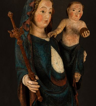 Zdjęcie nr 6: Rzeźba drążona, ukazująca Matkę Boską z Dzieciątkiem. Maria ustawiona frontalnie, w delikatnym kontrapoście, na lewym ręku trzyma Dzieciątko, w prawym dzierży berło. Twarz okrągła z wysokim czołem, drobnymi ustami i małymi oczami o delikatnie zarysowanych łukach brwiowych. Włosy jasne, ułożone w skręcone pukle spływające na plecy. Maria ubrana jest w białą suknię zdobioną drobnymi, niebieskimi gwiazdkami, ciemnobłękitny płaszcz z bordową podszewką spięty na piersi oraz spiczaste, brązowe buty. Na głowie ma założony ciemnoniebieski welon z bordową podszewką, spływający na ramiona i piersi oraz brązową podstawę do niezachowanej korony. Draperia szat miękka o wyraźnie zaznaczonych, licznych fałdach misowych i kaskadowych. Dzieciątko ukazane w pozycji siedzącej, zwrócone w prawo. W lewej dłoni trzyma jabłko królewskie, a prawą wyprostowaną podnosi na wysokość tułowia. Twarz pełna o dziecięcych rysach z małymi ustami, okolona krótkimi i kędzierzawymi włosami. Polichromia w odsłoniętych partiach ciała naturalistyczna, berło polichromowane na brązowo.