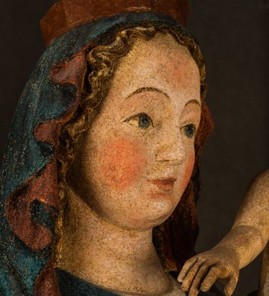 Zdjęcie nr 15: Rzeźba drążona, ukazująca Matkę Boską z Dzieciątkiem. Maria ustawiona frontalnie, w delikatnym kontrapoście, na lewym ręku trzyma Dzieciątko, w prawym dzierży berło. Twarz okrągła z wysokim czołem, drobnymi ustami i małymi oczami o delikatnie zarysowanych łukach brwiowych. Włosy jasne, ułożone w skręcone pukle spływające na plecy. Maria ubrana jest w białą suknię zdobioną drobnymi, niebieskimi gwiazdkami, ciemnobłękitny płaszcz z bordową podszewką spięty na piersi oraz spiczaste, brązowe buty. Na głowie ma założony ciemnoniebieski welon z bordową podszewką, spływający na ramiona i piersi oraz brązową podstawę do niezachowanej korony. Draperia szat miękka o wyraźnie zaznaczonych, licznych fałdach misowych i kaskadowych. Dzieciątko ukazane w pozycji siedzącej, zwrócone w prawo. W lewej dłoni trzyma jabłko królewskie, a prawą wyprostowaną podnosi na wysokość tułowia. Twarz pełna o dziecięcych rysach z małymi ustami, okolona krótkimi i kędzierzawymi włosami. Polichromia w odsłoniętych partiach ciała naturalistyczna, berło polichromowane na brązowo.