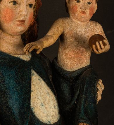 Zdjęcie nr 8: Rzeźba drążona, ukazująca Matkę Boską z Dzieciątkiem. Maria ustawiona frontalnie, w delikatnym kontrapoście, na lewym ręku trzyma Dzieciątko, w prawym dzierży berło. Twarz okrągła z wysokim czołem, drobnymi ustami i małymi oczami o delikatnie zarysowanych łukach brwiowych. Włosy jasne, ułożone w skręcone pukle spływające na plecy. Maria ubrana jest w białą suknię zdobioną drobnymi, niebieskimi gwiazdkami, ciemnobłękitny płaszcz z bordową podszewką spięty na piersi oraz spiczaste, brązowe buty. Na głowie ma założony ciemnoniebieski welon z bordową podszewką, spływający na ramiona i piersi oraz brązową podstawę do niezachowanej korony. Draperia szat miękka o wyraźnie zaznaczonych, licznych fałdach misowych i kaskadowych. Dzieciątko ukazane w pozycji siedzącej, zwrócone w prawo. W lewej dłoni trzyma jabłko królewskie, a prawą wyprostowaną podnosi na wysokość tułowia. Twarz pełna o dziecięcych rysach z małymi ustami, okolona krótkimi i kędzierzawymi włosami. Polichromia w odsłoniętych partiach ciała naturalistyczna, berło polichromowane na brązowo.