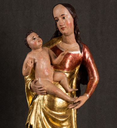 Zdjęcie nr 1: Całopostaciowa, pełnoplastyczna figura Madonny z Dzieciątkiem stojącej w wydatnym kontrapoście na podstawie o wykroju w kształcie półkola z parą wklęsek. Sylwetkę Marii charakteryzuje S-kształtny układ. Zwróconą w trzech czwartych w prawo, lekko przechyloną w bok głowę charakteryzują długie, ciemne, kręcone włosy opadające na plecy i lewe ramię oraz pociągła, owalna twarz o bardzo wysokim czole, łagodnych lukach ciemnych brwi, migdałowatych oczach, długim, zaokrąglonym na końcu nosie, pełnych, zaróżowionych policzkach, kształtnych ustach i zaokrąglonym podbródku. Długą szyję uwydatnia głęboki, półkolisty dekolt długiej, czerwonej sukni ze srebrnymi lamówkami, o długich, wąskich rękawach i ściśle przylegającej do tułowia. Sylwetkę ciasno osłania złocony płaszcz narzucony na prawe ramię osłaniając rękę talię i nogi do wysokości łydek. Spod sukni widoczne są ciemnobrązowe, spiczaste buty. Draperie cechuje dekoracyjny układ fałdowań w postaci spiętrzonej kaskady drobnych fałd rurkowych wzdłuż prawego biodra i nogi Marii oraz 3 promieniście opadających, C-kształtnych załamań. Nieco masywniejsze fałdy w dolnej partii sukni załamują się ostrymi formami pod wpływem styku z obuwiem i podłożem. Pod stopami sierp księżyca.  Maria prawą ręką podtrzymuje siedzące, zwrócone w trzech czwartych w lewo Dzieciątko lewą dłonią ujmując jego stopy. Jego nagą sylwetkę charakteryzuje stosunkowo sumaryczny modelunek ciała. Lekko odchyloną do tyłu głowę charakteryzuje owalna twarz o pełnych, zaokrąglonych rysach, z lekko wypukłym czołem, wyrazistymi łukami ciemnych, opadających brwi, dużymi, ciemnymi oczami, krótkim, lekko zadartym nosem, pełnymi ustami, zaróżowionymi policzkami i wyraźnie zarysowanym podbródkiem. Włosy krótkie, ciemne, mocno skręcone z wyraźnym puklem nad czołem, szyja krótka i szeroka. Zgięte w łokciach ręce uniesione są na wysokości klatki piersiowej, prawa bliżej sylwetki w geście błogosławieństwa, lewa nieco wysunięta do przodu z dłonią odwróconą ku górze. Prawa noga wyprostowana, lewa lekko zgięta w kolanie.       