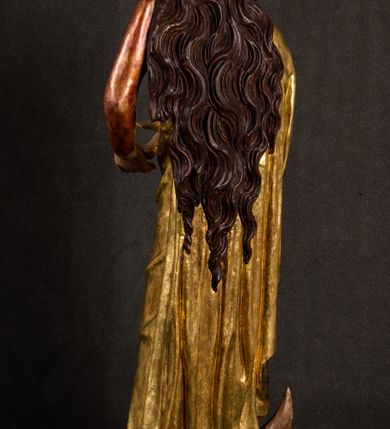 Zdjęcie nr 16: Całopostaciowa, pełnoplastyczna figura Madonny z Dzieciątkiem stojącej w wydatnym kontrapoście na podstawie o wykroju w kształcie półkola z parą wklęsek. Sylwetkę Marii charakteryzuje S-kształtny układ. Zwróconą w trzech czwartych w prawo, lekko przechyloną w bok głowę charakteryzują długie, ciemne, kręcone włosy opadające na plecy i lewe ramię oraz pociągła, owalna twarz o bardzo wysokim czole, łagodnych lukach ciemnych brwi, migdałowatych oczach, długim, zaokrąglonym na końcu nosie, pełnych, zaróżowionych policzkach, kształtnych ustach i zaokrąglonym podbródku. Długą szyję uwydatnia głęboki, półkolisty dekolt długiej, czerwonej sukni ze srebrnymi lamówkami, o długich, wąskich rękawach i ściśle przylegającej do tułowia. Sylwetkę ciasno osłania złocony płaszcz narzucony na prawe ramię osłaniając rękę talię i nogi do wysokości łydek. Spod sukni widoczne są ciemnobrązowe, spiczaste buty. Draperie cechuje dekoracyjny układ fałdowań w postaci spiętrzonej kaskady drobnych fałd rurkowych wzdłuż prawego biodra i nogi Marii oraz 3 promieniście opadających, C-kształtnych załamań. Nieco masywniejsze fałdy w dolnej partii sukni załamują się ostrymi formami pod wpływem styku z obuwiem i podłożem. Pod stopami sierp księżyca.  Maria prawą ręką podtrzymuje siedzące, zwrócone w trzech czwartych w lewo Dzieciątko lewą dłonią ujmując jego stopy. Jego nagą sylwetkę charakteryzuje stosunkowo sumaryczny modelunek ciała. Lekko odchyloną do tyłu głowę charakteryzuje owalna twarz o pełnych, zaokrąglonych rysach, z lekko wypukłym czołem, wyrazistymi łukami ciemnych, opadających brwi, dużymi, ciemnymi oczami, krótkim, lekko zadartym nosem, pełnymi ustami, zaróżowionymi policzkami i wyraźnie zarysowanym podbródkiem. Włosy krótkie, ciemne, mocno skręcone z wyraźnym puklem nad czołem, szyja krótka i szeroka. Zgięte w łokciach ręce uniesione są na wysokości klatki piersiowej, prawa bliżej sylwetki w geście błogosławieństwa, lewa nieco wysunięta do przodu z dłonią odwróconą ku górze. Prawa noga wyprostowana, lewa lekko zgięta w kolanie.       