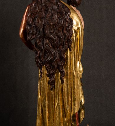 Zdjęcie nr 17: Całopostaciowa, pełnoplastyczna figura Madonny z Dzieciątkiem stojącej w wydatnym kontrapoście na podstawie o wykroju w kształcie półkola z parą wklęsek. Sylwetkę Marii charakteryzuje S-kształtny układ. Zwróconą w trzech czwartych w prawo, lekko przechyloną w bok głowę charakteryzują długie, ciemne, kręcone włosy opadające na plecy i lewe ramię oraz pociągła, owalna twarz o bardzo wysokim czole, łagodnych lukach ciemnych brwi, migdałowatych oczach, długim, zaokrąglonym na końcu nosie, pełnych, zaróżowionych policzkach, kształtnych ustach i zaokrąglonym podbródku. Długą szyję uwydatnia głęboki, półkolisty dekolt długiej, czerwonej sukni ze srebrnymi lamówkami, o długich, wąskich rękawach i ściśle przylegającej do tułowia. Sylwetkę ciasno osłania złocony płaszcz narzucony na prawe ramię osłaniając rękę talię i nogi do wysokości łydek. Spod sukni widoczne są ciemnobrązowe, spiczaste buty. Draperie cechuje dekoracyjny układ fałdowań w postaci spiętrzonej kaskady drobnych fałd rurkowych wzdłuż prawego biodra i nogi Marii oraz 3 promieniście opadających, C-kształtnych załamań. Nieco masywniejsze fałdy w dolnej partii sukni załamują się ostrymi formami pod wpływem styku z obuwiem i podłożem. Pod stopami sierp księżyca.  Maria prawą ręką podtrzymuje siedzące, zwrócone w trzech czwartych w lewo Dzieciątko lewą dłonią ujmując jego stopy. Jego nagą sylwetkę charakteryzuje stosunkowo sumaryczny modelunek ciała. Lekko odchyloną do tyłu głowę charakteryzuje owalna twarz o pełnych, zaokrąglonych rysach, z lekko wypukłym czołem, wyrazistymi łukami ciemnych, opadających brwi, dużymi, ciemnymi oczami, krótkim, lekko zadartym nosem, pełnymi ustami, zaróżowionymi policzkami i wyraźnie zarysowanym podbródkiem. Włosy krótkie, ciemne, mocno skręcone z wyraźnym puklem nad czołem, szyja krótka i szeroka. Zgięte w łokciach ręce uniesione są na wysokości klatki piersiowej, prawa bliżej sylwetki w geście błogosławieństwa, lewa nieco wysunięta do przodu z dłonią odwróconą ku górze. Prawa noga wyprostowana, lewa lekko zgięta w kolanie.       