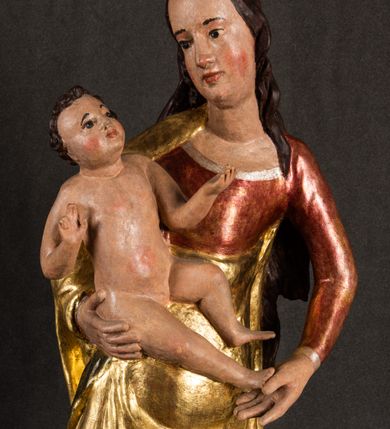 Zdjęcie nr 3: Całopostaciowa, pełnoplastyczna figura Madonny z Dzieciątkiem stojącej w wydatnym kontrapoście na podstawie o wykroju w kształcie półkola z parą wklęsek. Sylwetkę Marii charakteryzuje S-kształtny układ. Zwróconą w trzech czwartych w prawo, lekko przechyloną w bok głowę charakteryzują długie, ciemne, kręcone włosy opadające na plecy i lewe ramię oraz pociągła, owalna twarz o bardzo wysokim czole, łagodnych lukach ciemnych brwi, migdałowatych oczach, długim, zaokrąglonym na końcu nosie, pełnych, zaróżowionych policzkach, kształtnych ustach i zaokrąglonym podbródku. Długą szyję uwydatnia głęboki, półkolisty dekolt długiej, czerwonej sukni ze srebrnymi lamówkami, o długich, wąskich rękawach i ściśle przylegającej do tułowia. Sylwetkę ciasno osłania złocony płaszcz narzucony na prawe ramię osłaniając rękę talię i nogi do wysokości łydek. Spod sukni widoczne są ciemnobrązowe, spiczaste buty. Draperie cechuje dekoracyjny układ fałdowań w postaci spiętrzonej kaskady drobnych fałd rurkowych wzdłuż prawego biodra i nogi Marii oraz 3 promieniście opadających, C-kształtnych załamań. Nieco masywniejsze fałdy w dolnej partii sukni załamują się ostrymi formami pod wpływem styku z obuwiem i podłożem. Pod stopami sierp księżyca.  Maria prawą ręką podtrzymuje siedzące, zwrócone w trzech czwartych w lewo Dzieciątko lewą dłonią ujmując jego stopy. Jego nagą sylwetkę charakteryzuje stosunkowo sumaryczny modelunek ciała. Lekko odchyloną do tyłu głowę charakteryzuje owalna twarz o pełnych, zaokrąglonych rysach, z lekko wypukłym czołem, wyrazistymi łukami ciemnych, opadających brwi, dużymi, ciemnymi oczami, krótkim, lekko zadartym nosem, pełnymi ustami, zaróżowionymi policzkami i wyraźnie zarysowanym podbródkiem. Włosy krótkie, ciemne, mocno skręcone z wyraźnym puklem nad czołem, szyja krótka i szeroka. Zgięte w łokciach ręce uniesione są na wysokości klatki piersiowej, prawa bliżej sylwetki w geście błogosławieństwa, lewa nieco wysunięta do przodu z dłonią odwróconą ku górze. Prawa noga wyprostowana, lewa lekko zgięta w kolanie.       