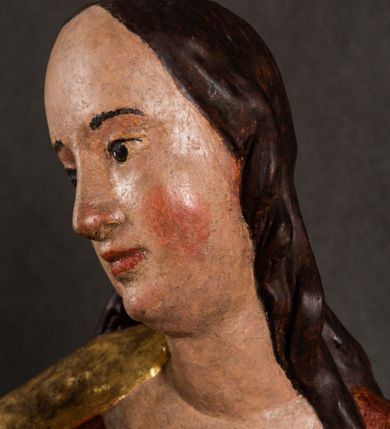 Zdjęcie nr 10: Całopostaciowa, pełnoplastyczna figura Madonny z Dzieciątkiem stojącej w wydatnym kontrapoście na podstawie o wykroju w kształcie półkola z parą wklęsek. Sylwetkę Marii charakteryzuje S-kształtny układ. Zwróconą w trzech czwartych w prawo, lekko przechyloną w bok głowę charakteryzują długie, ciemne, kręcone włosy opadające na plecy i lewe ramię oraz pociągła, owalna twarz o bardzo wysokim czole, łagodnych lukach ciemnych brwi, migdałowatych oczach, długim, zaokrąglonym na końcu nosie, pełnych, zaróżowionych policzkach, kształtnych ustach i zaokrąglonym podbródku. Długą szyję uwydatnia głęboki, półkolisty dekolt długiej, czerwonej sukni ze srebrnymi lamówkami, o długich, wąskich rękawach i ściśle przylegającej do tułowia. Sylwetkę ciasno osłania złocony płaszcz narzucony na prawe ramię osłaniając rękę talię i nogi do wysokości łydek. Spod sukni widoczne są ciemnobrązowe, spiczaste buty. Draperie cechuje dekoracyjny układ fałdowań w postaci spiętrzonej kaskady drobnych fałd rurkowych wzdłuż prawego biodra i nogi Marii oraz 3 promieniście opadających, C-kształtnych załamań. Nieco masywniejsze fałdy w dolnej partii sukni załamują się ostrymi formami pod wpływem styku z obuwiem i podłożem. Pod stopami sierp księżyca.  Maria prawą ręką podtrzymuje siedzące, zwrócone w trzech czwartych w lewo Dzieciątko lewą dłonią ujmując jego stopy. Jego nagą sylwetkę charakteryzuje stosunkowo sumaryczny modelunek ciała. Lekko odchyloną do tyłu głowę charakteryzuje owalna twarz o pełnych, zaokrąglonych rysach, z lekko wypukłym czołem, wyrazistymi łukami ciemnych, opadających brwi, dużymi, ciemnymi oczami, krótkim, lekko zadartym nosem, pełnymi ustami, zaróżowionymi policzkami i wyraźnie zarysowanym podbródkiem. Włosy krótkie, ciemne, mocno skręcone z wyraźnym puklem nad czołem, szyja krótka i szeroka. Zgięte w łokciach ręce uniesione są na wysokości klatki piersiowej, prawa bliżej sylwetki w geście błogosławieństwa, lewa nieco wysunięta do przodu z dłonią odwróconą ku górze. Prawa noga wyprostowana, lewa lekko zgięta w kolanie.       