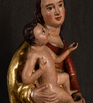 Zdjęcie nr 7: Całopostaciowa, pełnoplastyczna figura Madonny z Dzieciątkiem stojącej w wydatnym kontrapoście na podstawie o wykroju w kształcie półkola z parą wklęsek. Sylwetkę Marii charakteryzuje S-kształtny układ. Zwróconą w trzech czwartych w prawo, lekko przechyloną w bok głowę charakteryzują długie, ciemne, kręcone włosy opadające na plecy i lewe ramię oraz pociągła, owalna twarz o bardzo wysokim czole, łagodnych lukach ciemnych brwi, migdałowatych oczach, długim, zaokrąglonym na końcu nosie, pełnych, zaróżowionych policzkach, kształtnych ustach i zaokrąglonym podbródku. Długą szyję uwydatnia głęboki, półkolisty dekolt długiej, czerwonej sukni ze srebrnymi lamówkami, o długich, wąskich rękawach i ściśle przylegającej do tułowia. Sylwetkę ciasno osłania złocony płaszcz narzucony na prawe ramię osłaniając rękę talię i nogi do wysokości łydek. Spod sukni widoczne są ciemnobrązowe, spiczaste buty. Draperie cechuje dekoracyjny układ fałdowań w postaci spiętrzonej kaskady drobnych fałd rurkowych wzdłuż prawego biodra i nogi Marii oraz 3 promieniście opadających, C-kształtnych załamań. Nieco masywniejsze fałdy w dolnej partii sukni załamują się ostrymi formami pod wpływem styku z obuwiem i podłożem. Pod stopami sierp księżyca.  Maria prawą ręką podtrzymuje siedzące, zwrócone w trzech czwartych w lewo Dzieciątko lewą dłonią ujmując jego stopy. Jego nagą sylwetkę charakteryzuje stosunkowo sumaryczny modelunek ciała. Lekko odchyloną do tyłu głowę charakteryzuje owalna twarz o pełnych, zaokrąglonych rysach, z lekko wypukłym czołem, wyrazistymi łukami ciemnych, opadających brwi, dużymi, ciemnymi oczami, krótkim, lekko zadartym nosem, pełnymi ustami, zaróżowionymi policzkami i wyraźnie zarysowanym podbródkiem. Włosy krótkie, ciemne, mocno skręcone z wyraźnym puklem nad czołem, szyja krótka i szeroka. Zgięte w łokciach ręce uniesione są na wysokości klatki piersiowej, prawa bliżej sylwetki w geście błogosławieństwa, lewa nieco wysunięta do przodu z dłonią odwróconą ku górze. Prawa noga wyprostowana, lewa lekko zgięta w kolanie.       