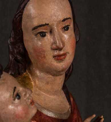 Zdjęcie nr 11: Całopostaciowa, pełnoplastyczna figura Madonny z Dzieciątkiem stojącej w wydatnym kontrapoście na podstawie o wykroju w kształcie półkola z parą wklęsek. Sylwetkę Marii charakteryzuje S-kształtny układ. Zwróconą w trzech czwartych w prawo, lekko przechyloną w bok głowę charakteryzują długie, ciemne, kręcone włosy opadające na plecy i lewe ramię oraz pociągła, owalna twarz o bardzo wysokim czole, łagodnych lukach ciemnych brwi, migdałowatych oczach, długim, zaokrąglonym na końcu nosie, pełnych, zaróżowionych policzkach, kształtnych ustach i zaokrąglonym podbródku. Długą szyję uwydatnia głęboki, półkolisty dekolt długiej, czerwonej sukni ze srebrnymi lamówkami, o długich, wąskich rękawach i ściśle przylegającej do tułowia. Sylwetkę ciasno osłania złocony płaszcz narzucony na prawe ramię osłaniając rękę talię i nogi do wysokości łydek. Spod sukni widoczne są ciemnobrązowe, spiczaste buty. Draperie cechuje dekoracyjny układ fałdowań w postaci spiętrzonej kaskady drobnych fałd rurkowych wzdłuż prawego biodra i nogi Marii oraz 3 promieniście opadających, C-kształtnych załamań. Nieco masywniejsze fałdy w dolnej partii sukni załamują się ostrymi formami pod wpływem styku z obuwiem i podłożem. Pod stopami sierp księżyca.  Maria prawą ręką podtrzymuje siedzące, zwrócone w trzech czwartych w lewo Dzieciątko lewą dłonią ujmując jego stopy. Jego nagą sylwetkę charakteryzuje stosunkowo sumaryczny modelunek ciała. Lekko odchyloną do tyłu głowę charakteryzuje owalna twarz o pełnych, zaokrąglonych rysach, z lekko wypukłym czołem, wyrazistymi łukami ciemnych, opadających brwi, dużymi, ciemnymi oczami, krótkim, lekko zadartym nosem, pełnymi ustami, zaróżowionymi policzkami i wyraźnie zarysowanym podbródkiem. Włosy krótkie, ciemne, mocno skręcone z wyraźnym puklem nad czołem, szyja krótka i szeroka. Zgięte w łokciach ręce uniesione są na wysokości klatki piersiowej, prawa bliżej sylwetki w geście błogosławieństwa, lewa nieco wysunięta do przodu z dłonią odwróconą ku górze. Prawa noga wyprostowana, lewa lekko zgięta w kolanie.       