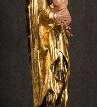 Zdjęcie nr 14: Całopostaciowa, pełnoplastyczna figura Madonny z Dzieciątkiem stojącej w wydatnym kontrapoście na podstawie o wykroju w kształcie półkola z parą wklęsek. Sylwetkę Marii charakteryzuje S-kształtny układ. Zwróconą w trzech czwartych w prawo, lekko przechyloną w bok głowę charakteryzują długie, ciemne, kręcone włosy opadające na plecy i lewe ramię oraz pociągła, owalna twarz o bardzo wysokim czole, łagodnych lukach ciemnych brwi, migdałowatych oczach, długim, zaokrąglonym na końcu nosie, pełnych, zaróżowionych policzkach, kształtnych ustach i zaokrąglonym podbródku. Długą szyję uwydatnia głęboki, półkolisty dekolt długiej, czerwonej sukni ze srebrnymi lamówkami, o długich, wąskich rękawach i ściśle przylegającej do tułowia. Sylwetkę ciasno osłania złocony płaszcz narzucony na prawe ramię osłaniając rękę talię i nogi do wysokości łydek. Spod sukni widoczne są ciemnobrązowe, spiczaste buty. Draperie cechuje dekoracyjny układ fałdowań w postaci spiętrzonej kaskady drobnych fałd rurkowych wzdłuż prawego biodra i nogi Marii oraz 3 promieniście opadających, C-kształtnych załamań. Nieco masywniejsze fałdy w dolnej partii sukni załamują się ostrymi formami pod wpływem styku z obuwiem i podłożem. Pod stopami sierp księżyca.  Maria prawą ręką podtrzymuje siedzące, zwrócone w trzech czwartych w lewo Dzieciątko lewą dłonią ujmując jego stopy. Jego nagą sylwetkę charakteryzuje stosunkowo sumaryczny modelunek ciała. Lekko odchyloną do tyłu głowę charakteryzuje owalna twarz o pełnych, zaokrąglonych rysach, z lekko wypukłym czołem, wyrazistymi łukami ciemnych, opadających brwi, dużymi, ciemnymi oczami, krótkim, lekko zadartym nosem, pełnymi ustami, zaróżowionymi policzkami i wyraźnie zarysowanym podbródkiem. Włosy krótkie, ciemne, mocno skręcone z wyraźnym puklem nad czołem, szyja krótka i szeroka. Zgięte w łokciach ręce uniesione są na wysokości klatki piersiowej, prawa bliżej sylwetki w geście błogosławieństwa, lewa nieco wysunięta do przodu z dłonią odwróconą ku górze. Prawa noga wyprostowana, lewa lekko zgięta w kolanie.       