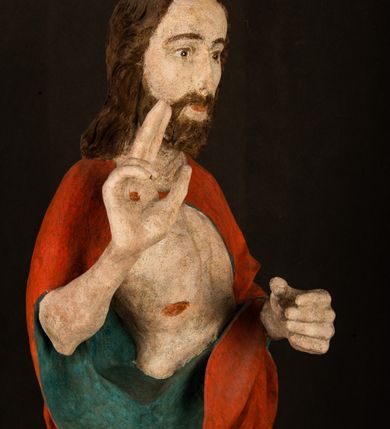 Zdjęcie nr 3: Pełnoplastyczna rzeźba ukazuje frontalnie w całej postaci zmartwychwstałego Chrystusa stojącego w kontrapoście na niewielkim wzgórku. Jego prawa noga jest nieco wysunięta i zgięta w kolanie. Zmartwychwstały unosi w geście zwycięstwa prawą rękę zgiętą w łokciu, lewą zaś uniesioną na wysokość piersi trzyma proporzec. Zbawiciel ma nieproporcjonalnie duże dłonie. Na rękach, stopach i boku widać ślady po męce. Chrystus ma mocno pociągłą twarz okoloną, krótkim, brązowym zarostem i brązowe włosy spływające na plecy. Jego twarz o jasnej karnacji charakteryzuje wysokie czoło, prosty nos i wydatne usta oraz szeroko otwarte ciemne oczy o spojrzeniu skierowanym przed siebie. Jezus ubrany jest w spięty pod szyją czerwony płaszcz podbity ciemną zielenią grynszpanową sięgający łydek z prawą połą podwiniętą przy lewym boku. Płaszcz odsłania mocno taliowany nagi tors z widocznym przebitym prawym bokiem.  