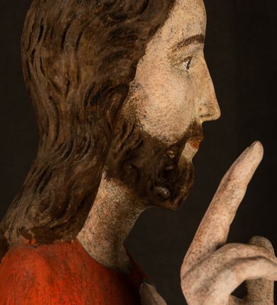 Zdjęcie nr 6: Pełnoplastyczna rzeźba ukazuje frontalnie w całej postaci zmartwychwstałego Chrystusa stojącego w kontrapoście na niewielkim wzgórku. Jego prawa noga jest nieco wysunięta i zgięta w kolanie. Zmartwychwstały unosi w geście zwycięstwa prawą rękę zgiętą w łokciu, lewą zaś uniesioną na wysokość piersi trzyma proporzec. Zbawiciel ma nieproporcjonalnie duże dłonie. Na rękach, stopach i boku widać ślady po męce. Chrystus ma mocno pociągłą twarz okoloną, krótkim, brązowym zarostem i brązowe włosy spływające na plecy. Jego twarz o jasnej karnacji charakteryzuje wysokie czoło, prosty nos i wydatne usta oraz szeroko otwarte ciemne oczy o spojrzeniu skierowanym przed siebie. Jezus ubrany jest w spięty pod szyją czerwony płaszcz podbity ciemną zielenią grynszpanową sięgający łydek z prawą połą podwiniętą przy lewym boku. Płaszcz odsłania mocno taliowany nagi tors z widocznym przebitym prawym bokiem.  