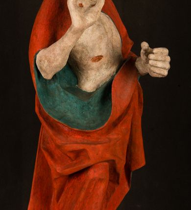 Zdjęcie nr 8: Pełnoplastyczna rzeźba ukazuje frontalnie w całej postaci zmartwychwstałego Chrystusa stojącego w kontrapoście na niewielkim wzgórku. Jego prawa noga jest nieco wysunięta i zgięta w kolanie. Zmartwychwstały unosi w geście zwycięstwa prawą rękę zgiętą w łokciu, lewą zaś uniesioną na wysokość piersi trzyma proporzec. Zbawiciel ma nieproporcjonalnie duże dłonie. Na rękach, stopach i boku widać ślady po męce. Chrystus ma mocno pociągłą twarz okoloną, krótkim, brązowym zarostem i brązowe włosy spływające na plecy. Jego twarz o jasnej karnacji charakteryzuje wysokie czoło, prosty nos i wydatne usta oraz szeroko otwarte ciemne oczy o spojrzeniu skierowanym przed siebie. Jezus ubrany jest w spięty pod szyją czerwony płaszcz podbity ciemną zielenią grynszpanową sięgający łydek z prawą połą podwiniętą przy lewym boku. Płaszcz odsłania mocno taliowany nagi tors z widocznym przebitym prawym bokiem.  