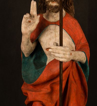 Zdjęcie nr 2: Pełnoplastyczna rzeźba ukazuje frontalnie w całej postaci zmartwychwstałego Chrystusa stojącego w kontrapoście na niewielkim wzgórku. Jego prawa noga jest nieco wysunięta i zgięta w kolanie. Zmartwychwstały unosi w geście zwycięstwa prawą rękę zgiętą w łokciu, lewą zaś uniesioną na wysokość piersi trzyma proporzec. Zbawiciel ma nieproporcjonalnie duże dłonie. Na rękach, stopach i boku widać ślady po męce. Chrystus ma mocno pociągłą twarz okoloną, krótkim, brązowym zarostem i brązowe włosy spływające na plecy. Jego twarz o jasnej karnacji charakteryzuje wysokie czoło, prosty nos i wydatne usta oraz szeroko otwarte ciemne oczy o spojrzeniu skierowanym przed siebie. Jezus ubrany jest w spięty pod szyją czerwony płaszcz podbity ciemną zielenią grynszpanową sięgający łydek z prawą połą podwiniętą przy lewym boku. Płaszcz odsłania mocno taliowany nagi tors z widocznym przebitym prawym bokiem.  