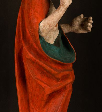 Zdjęcie nr 9: Pełnoplastyczna rzeźba ukazuje frontalnie w całej postaci zmartwychwstałego Chrystusa stojącego w kontrapoście na niewielkim wzgórku. Jego prawa noga jest nieco wysunięta i zgięta w kolanie. Zmartwychwstały unosi w geście zwycięstwa prawą rękę zgiętą w łokciu, lewą zaś uniesioną na wysokość piersi trzyma proporzec. Zbawiciel ma nieproporcjonalnie duże dłonie. Na rękach, stopach i boku widać ślady po męce. Chrystus ma mocno pociągłą twarz okoloną, krótkim, brązowym zarostem i brązowe włosy spływające na plecy. Jego twarz o jasnej karnacji charakteryzuje wysokie czoło, prosty nos i wydatne usta oraz szeroko otwarte ciemne oczy o spojrzeniu skierowanym przed siebie. Jezus ubrany jest w spięty pod szyją czerwony płaszcz podbity ciemną zielenią grynszpanową sięgający łydek z prawą połą podwiniętą przy lewym boku. Płaszcz odsłania mocno taliowany nagi tors z widocznym przebitym prawym bokiem.  