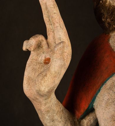 Zdjęcie nr 4: Pełnoplastyczna rzeźba ukazuje frontalnie w całej postaci zmartwychwstałego Chrystusa stojącego w kontrapoście na niewielkim wzgórku. Jego prawa noga jest nieco wysunięta i zgięta w kolanie. Zmartwychwstały unosi w geście zwycięstwa prawą rękę zgiętą w łokciu, lewą zaś uniesioną na wysokość piersi trzyma proporzec. Zbawiciel ma nieproporcjonalnie duże dłonie. Na rękach, stopach i boku widać ślady po męce. Chrystus ma mocno pociągłą twarz okoloną, krótkim, brązowym zarostem i brązowe włosy spływające na plecy. Jego twarz o jasnej karnacji charakteryzuje wysokie czoło, prosty nos i wydatne usta oraz szeroko otwarte ciemne oczy o spojrzeniu skierowanym przed siebie. Jezus ubrany jest w spięty pod szyją czerwony płaszcz podbity ciemną zielenią grynszpanową sięgający łydek z prawą połą podwiniętą przy lewym boku. Płaszcz odsłania mocno taliowany nagi tors z widocznym przebitym prawym bokiem.  