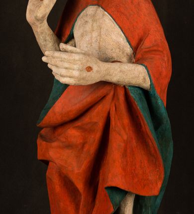 Zdjęcie nr 7: Pełnoplastyczna rzeźba ukazuje frontalnie w całej postaci zmartwychwstałego Chrystusa stojącego w kontrapoście na niewielkim wzgórku. Jego prawa noga jest nieco wysunięta i zgięta w kolanie. Zmartwychwstały unosi w geście zwycięstwa prawą rękę zgiętą w łokciu, lewą zaś uniesioną na wysokość piersi trzyma proporzec. Zbawiciel ma nieproporcjonalnie duże dłonie. Na rękach, stopach i boku widać ślady po męce. Chrystus ma mocno pociągłą twarz okoloną, krótkim, brązowym zarostem i brązowe włosy spływające na plecy. Jego twarz o jasnej karnacji charakteryzuje wysokie czoło, prosty nos i wydatne usta oraz szeroko otwarte ciemne oczy o spojrzeniu skierowanym przed siebie. Jezus ubrany jest w spięty pod szyją czerwony płaszcz podbity ciemną zielenią grynszpanową sięgający łydek z prawą połą podwiniętą przy lewym boku. Płaszcz odsłania mocno taliowany nagi tors z widocznym przebitym prawym bokiem.  