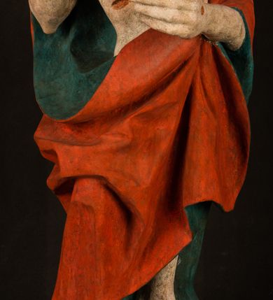 Zdjęcie nr 13: Pełnoplastyczna rzeźba ukazuje frontalnie w całej postaci zmartwychwstałego Chrystusa stojącego w kontrapoście na niewielkim wzgórku. Jego prawa noga jest nieco wysunięta i zgięta w kolanie. Zmartwychwstały unosi w geście zwycięstwa prawą rękę zgiętą w łokciu, lewą zaś uniesioną na wysokość piersi trzyma proporzec. Zbawiciel ma nieproporcjonalnie duże dłonie. Na rękach, stopach i boku widać ślady po męce. Chrystus ma mocno pociągłą twarz okoloną, krótkim, brązowym zarostem i brązowe włosy spływające na plecy. Jego twarz o jasnej karnacji charakteryzuje wysokie czoło, prosty nos i wydatne usta oraz szeroko otwarte ciemne oczy o spojrzeniu skierowanym przed siebie. Jezus ubrany jest w spięty pod szyją czerwony płaszcz podbity ciemną zielenią grynszpanową sięgający łydek z prawą połą podwiniętą przy lewym boku. Płaszcz odsłania mocno taliowany nagi tors z widocznym przebitym prawym bokiem.  