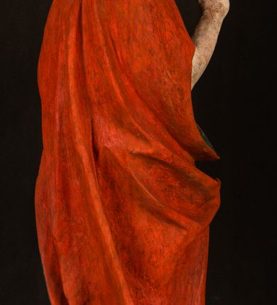 Zdjęcie nr 12: Pełnoplastyczna rzeźba ukazuje frontalnie w całej postaci zmartwychwstałego Chrystusa stojącego w kontrapoście na niewielkim wzgórku. Jego prawa noga jest nieco wysunięta i zgięta w kolanie. Zmartwychwstały unosi w geście zwycięstwa prawą rękę zgiętą w łokciu, lewą zaś uniesioną na wysokość piersi trzyma proporzec. Zbawiciel ma nieproporcjonalnie duże dłonie. Na rękach, stopach i boku widać ślady po męce. Chrystus ma mocno pociągłą twarz okoloną, krótkim, brązowym zarostem i brązowe włosy spływające na plecy. Jego twarz o jasnej karnacji charakteryzuje wysokie czoło, prosty nos i wydatne usta oraz szeroko otwarte ciemne oczy o spojrzeniu skierowanym przed siebie. Jezus ubrany jest w spięty pod szyją czerwony płaszcz podbity ciemną zielenią grynszpanową sięgający łydek z prawą połą podwiniętą przy lewym boku. Płaszcz odsłania mocno taliowany nagi tors z widocznym przebitym prawym bokiem.  