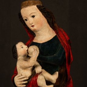 Zdjęcie nr 1: Rzeźba drążona, w pełni polichromowana. Pełnopostaciowe przedstawienie Marii karmiącej Dzieciątko Jezus. Matka Boska ukazana frontalnie, w pozycji siedzącej, trzyma na kolanach małego Jezusa, którego karmi piersią. Prawą ręką podtrzymuje Dzieciątko, lewą podaje mu pierś. Przedstawiona jako młoda kobieta o szerokiej, owalnej twarzy o wysokim czole i długich, ciemnych włosach. Oczy migdałowate, wpatrzone przed siebie. Cieńkie, łukowate brwi, niewielkie usta. Na głowie charakterystyczne podwyższenie – zapewne ślad po mocowaniu korony. Maria ubrana jest w ciemnogranatową, obcisłą suknię z długimi rękawami oraz czerwony płaszcz. Poła płaszcza okrywa również biodra Dzieciątka. Spod fałdów szat widoczne są czarne trzewiki o spiczastych noskach. Dzieciątko ukazane w pozycji siedzącej z głową uniesioną do góry, wyciągniętymi do przodu nóżkami i lewą ręką trzymającą pierś Marii. Twarz pełna z szeroko otwartymi oczami wpatrzonymi w matkę i zaróżowionymi policzkami. Włosy, krótkie, ciemne.