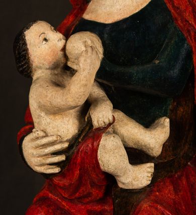 Zdjęcie nr 8: Rzeźba drążona, w pełni polichromowana. Pełnopostaciowe przedstawienie Marii karmiącej Dzieciątko Jezus. Matka Boska ukazana frontalnie, w pozycji siedzącej, trzyma na kolanach małego Jezusa, którego karmi piersią. Prawą ręką podtrzymuje Dzieciątko, lewą podaje mu pierś. Przedstawiona jako młoda kobieta o szerokiej, owalnej twarzy o wysokim czole i długich, ciemnych włosach. Oczy migdałowate, wpatrzone przed siebie. Cieńkie, łukowate brwi, niewielkie usta. Na głowie charakterystyczne podwyższenie – zapewne ślad po mocowaniu korony. Maria ubrana jest w ciemnogranatową, obcisłą suknię z długimi rękawami oraz czerwony płaszcz. Poła płaszcza okrywa również biodra Dzieciątka. Spod fałdów szat widoczne są czarne trzewiki o spiczastych noskach. Dzieciątko ukazane w pozycji siedzącej z głową uniesioną do góry, wyciągniętymi do przodu nóżkami i lewą ręką trzymającą pierś Marii. Twarz pełna z szeroko otwartymi oczami wpatrzonymi w matkę i zaróżowionymi policzkami. Włosy, krótkie, ciemne.