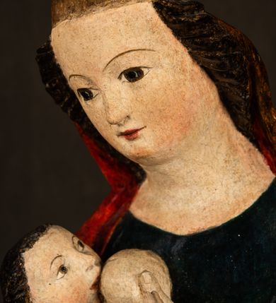 Zdjęcie nr 9: Rzeźba drążona, w pełni polichromowana. Pełnopostaciowe przedstawienie Marii karmiącej Dzieciątko Jezus. Matka Boska ukazana frontalnie, w pozycji siedzącej, trzyma na kolanach małego Jezusa, którego karmi piersią. Prawą ręką podtrzymuje Dzieciątko, lewą podaje mu pierś. Przedstawiona jako młoda kobieta o szerokiej, owalnej twarzy o wysokim czole i długich, ciemnych włosach. Oczy migdałowate, wpatrzone przed siebie. Cieńkie, łukowate brwi, niewielkie usta. Na głowie charakterystyczne podwyższenie – zapewne ślad po mocowaniu korony. Maria ubrana jest w ciemnogranatową, obcisłą suknię z długimi rękawami oraz czerwony płaszcz. Poła płaszcza okrywa również biodra Dzieciątka. Spod fałdów szat widoczne są czarne trzewiki o spiczastych noskach. Dzieciątko ukazane w pozycji siedzącej z głową uniesioną do góry, wyciągniętymi do przodu nóżkami i lewą ręką trzymającą pierś Marii. Twarz pełna z szeroko otwartymi oczami wpatrzonymi w matkę i zaróżowionymi policzkami. Włosy, krótkie, ciemne.