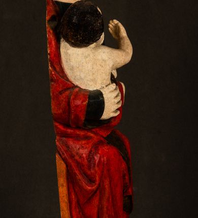 Zdjęcie nr 4: Rzeźba drążona, w pełni polichromowana. Pełnopostaciowe przedstawienie Marii karmiącej Dzieciątko Jezus. Matka Boska ukazana frontalnie, w pozycji siedzącej, trzyma na kolanach małego Jezusa, którego karmi piersią. Prawą ręką podtrzymuje Dzieciątko, lewą podaje mu pierś. Przedstawiona jako młoda kobieta o szerokiej, owalnej twarzy o wysokim czole i długich, ciemnych włosach. Oczy migdałowate, wpatrzone przed siebie. Cieńkie, łukowate brwi, niewielkie usta. Na głowie charakterystyczne podwyższenie – zapewne ślad po mocowaniu korony. Maria ubrana jest w ciemnogranatową, obcisłą suknię z długimi rękawami oraz czerwony płaszcz. Poła płaszcza okrywa również biodra Dzieciątka. Spod fałdów szat widoczne są czarne trzewiki o spiczastych noskach. Dzieciątko ukazane w pozycji siedzącej z głową uniesioną do góry, wyciągniętymi do przodu nóżkami i lewą ręką trzymającą pierś Marii. Twarz pełna z szeroko otwartymi oczami wpatrzonymi w matkę i zaróżowionymi policzkami. Włosy, krótkie, ciemne.