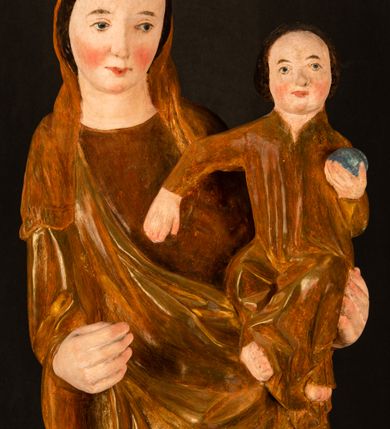 Zdjęcie nr 5: Rzeźba pełnoplastyczna, przyścienna, z tyłu wydrążona. Przedstawienie Matki Boskiej z Dzieciątkiem, ukazanej w całej postaci, frontalnie. Maria stoi w kontrapoście, esowato wygięta, z głową lekko przechyloną w lewo, podtrzymując Dzieciątko ręką wspartą na lewym biodrze. Twarz owalna, o subtelnych rysach, z wysokim czołem, regularnymi łukami brwiowymi i dużymi oczami, długim, wąskim nosem, małymi ustami i wydatnym podbródkiem. Ubrana w długą suknię i narzucony na ramiona płaszcz, przerzucony przez przód sylwetki i układający się poniżej piersi Marii sekwencją fałdów misowych i v-kształtnych. Na głowie źle zachowana chusta spływająca na ramiona. Dzieciątko siedzi na lewym przedramieniu Matki, ze skrzyżowanymi nóżkami, prawą dłonią dotykając piersi Marii, lewą trzyma glob. Twarz okrągła, o drobnych rysach, okolona krótkimi ciemnymi włosami. Jezus ubrany w długą sukienkę, spod której widać bose stopy.   