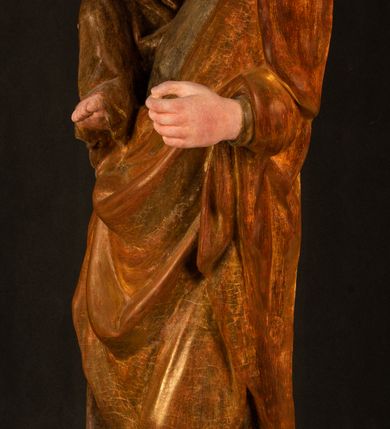 Zdjęcie nr 13: Rzeźba drążona, ustawiona na niewielkim, wielobocznym postumencie. Stojąca Maria ukazana frontalnie, w silnym kontrapoście z esowato wygiętym ciałem. Na lewej ręce podtrzymuje siedzące Dzieciątko, w prawej ręce ugiętej w łokciu i wyciągniętej do przodu najpewniej znajdowało się kiedyś berło.  Maria została ukazana jako młoda kobieta o owalnej twarzy, dużych, migdałowatych oczach, długim, prostym nosie i wyraźnie zaakcentowanych, dużych ustach. Karnacja jasna z rumieńcem zaznaczonym na policzkach i podbródku. Długie, jasne i falowane włosy częściowo zakryte chustą, symetrycznie okalają twarz postaci, spadając na jej ramiona. Maria jest ubrana w długą, sięgającą ziemi suknię, spod której widoczne są ostro zakończone czubki złotych butów oraz obszerny, złoty płaszcz tworzący ostro załamujące się fałdy na wysokości kolan Marii i formujący kaskadę wzdłuż prawego boku postaci. Na głowie Marii znajduje się biała chusta ze złota lamówką. Dzieciątko Jezus ukazane w pozycji siedzącej z lewą nogą wysuniętą wyraźnie do przodu. Prawą ręką wykonuje gest błogosławieństwa, w lewej trzyma niewielkie jabłko. Chłopiec o okrągłej, pulchnej twarzy i  krótkich, falowanych włosach spogląda przed siebie. Ubrany jest w wąską, suknię o długich rękawach, wykończoną przy dekolcie złotą lamówką. Spod sukni widoczne są bose stopy postaci. Karnacje postaci i część szat polichromowane, suknia Marii srebrzona, płaszcz i buty złocone.