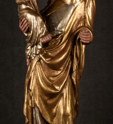 Zdjęcie nr 16: Rzeźba drążona, ustawiona na niewielkim, wielobocznym postumencie. Stojąca Maria ukazana frontalnie, w silnym kontrapoście z esowato wygiętym ciałem. Na lewej ręce podtrzymuje siedzące Dzieciątko, w prawej ręce ugiętej w łokciu i wyciągniętej do przodu najpewniej znajdowało się kiedyś berło.  Maria została ukazana jako młoda kobieta o owalnej twarzy, dużych, migdałowatych oczach, długim, prostym nosie i wyraźnie zaakcentowanych, dużych ustach. Karnacja jasna z rumieńcem zaznaczonym na policzkach i podbródku. Długie, jasne i falowane włosy częściowo zakryte chustą, symetrycznie okalają twarz postaci, spadając na jej ramiona. Maria jest ubrana w długą, sięgającą ziemi suknię, spod której widoczne są ostro zakończone czubki złotych butów oraz obszerny, złoty płaszcz tworzący ostro załamujące się fałdy na wysokości kolan Marii i formujący kaskadę wzdłuż prawego boku postaci. Na głowie Marii znajduje się biała chusta ze złota lamówką. Dzieciątko Jezus ukazane w pozycji siedzącej z lewą nogą wysuniętą wyraźnie do przodu. Prawą ręką wykonuje gest błogosławieństwa, w lewej trzyma niewielkie jabłko. Chłopiec o okrągłej, pulchnej twarzy i  krótkich, falowanych włosach spogląda przed siebie. Ubrany jest w wąską, suknię o długich rękawach, wykończoną przy dekolcie złotą lamówką. Spod sukni widoczne są bose stopy postaci. Karnacje postaci i część szat polichromowane, suknia Marii srebrzona, płaszcz i buty złocone.