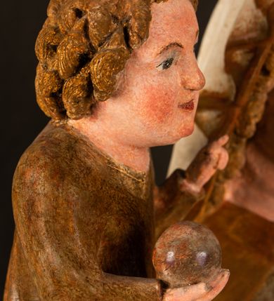 Zdjęcie nr 15: Rzeźba drążona, ustawiona na niewielkim, wielobocznym postumencie. Stojąca Maria ukazana frontalnie, w silnym kontrapoście z esowato wygiętym ciałem. Na lewej ręce podtrzymuje siedzące Dzieciątko, w prawej ręce ugiętej w łokciu i wyciągniętej do przodu najpewniej znajdowało się kiedyś berło.  Maria została ukazana jako młoda kobieta o owalnej twarzy, dużych, migdałowatych oczach, długim, prostym nosie i wyraźnie zaakcentowanych, dużych ustach. Karnacja jasna z rumieńcem zaznaczonym na policzkach i podbródku. Długie, jasne i falowane włosy częściowo zakryte chustą, symetrycznie okalają twarz postaci, spadając na jej ramiona. Maria jest ubrana w długą, sięgającą ziemi suknię, spod której widoczne są ostro zakończone czubki złotych butów oraz obszerny, złoty płaszcz tworzący ostro załamujące się fałdy na wysokości kolan Marii i formujący kaskadę wzdłuż prawego boku postaci. Na głowie Marii znajduje się biała chusta ze złota lamówką. Dzieciątko Jezus ukazane w pozycji siedzącej z lewą nogą wysuniętą wyraźnie do przodu. Prawą ręką wykonuje gest błogosławieństwa, w lewej trzyma niewielkie jabłko. Chłopiec o okrągłej, pulchnej twarzy i  krótkich, falowanych włosach spogląda przed siebie. Ubrany jest w wąską, suknię o długich rękawach, wykończoną przy dekolcie złotą lamówką. Spod sukni widoczne są bose stopy postaci. Karnacje postaci i część szat polichromowane, suknia Marii srebrzona, płaszcz i buty złocone.