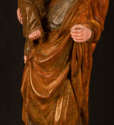 Zdjęcie nr 2: Rzeźba drążona, ustawiona na niewielkim, wielobocznym postumencie. Stojąca Maria ukazana frontalnie, w silnym kontrapoście z esowato wygiętym ciałem. Na lewej ręce podtrzymuje siedzące Dzieciątko, w prawej ręce ugiętej w łokciu i wyciągniętej do przodu najpewniej znajdowało się kiedyś berło.  Maria została ukazana jako młoda kobieta o owalnej twarzy, dużych, migdałowatych oczach, długim, prostym nosie i wyraźnie zaakcentowanych, dużych ustach. Karnacja jasna z rumieńcem zaznaczonym na policzkach i podbródku. Długie, jasne i falowane włosy częściowo zakryte chustą, symetrycznie okalają twarz postaci, spadając na jej ramiona. Maria jest ubrana w długą, sięgającą ziemi suknię, spod której widoczne są ostro zakończone czubki złotych butów oraz obszerny, złoty płaszcz tworzący ostro załamujące się fałdy na wysokości kolan Marii i formujący kaskadę wzdłuż prawego boku postaci. Na głowie Marii znajduje się biała chusta ze złota lamówką. Dzieciątko Jezus ukazane w pozycji siedzącej z lewą nogą wysuniętą wyraźnie do przodu. Prawą ręką wykonuje gest błogosławieństwa, w lewej trzyma niewielkie jabłko. Chłopiec o okrągłej, pulchnej twarzy i  krótkich, falowanych włosach spogląda przed siebie. Ubrany jest w wąską, suknię o długich rękawach, wykończoną przy dekolcie złotą lamówką. Spod sukni widoczne są bose stopy postaci. Karnacje postaci i część szat polichromowane, suknia Marii srebrzona, płaszcz i buty złocone.