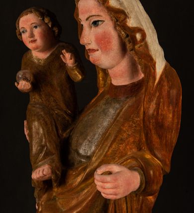 Zdjęcie nr 5: Rzeźba drążona, ustawiona na niewielkim, wielobocznym postumencie. Stojąca Maria ukazana frontalnie, w silnym kontrapoście z esowato wygiętym ciałem. Na lewej ręce podtrzymuje siedzące Dzieciątko, w prawej ręce ugiętej w łokciu i wyciągniętej do przodu najpewniej znajdowało się kiedyś berło.  Maria została ukazana jako młoda kobieta o owalnej twarzy, dużych, migdałowatych oczach, długim, prostym nosie i wyraźnie zaakcentowanych, dużych ustach. Karnacja jasna z rumieńcem zaznaczonym na policzkach i podbródku. Długie, jasne i falowane włosy częściowo zakryte chustą, symetrycznie okalają twarz postaci, spadając na jej ramiona. Maria jest ubrana w długą, sięgającą ziemi suknię, spod której widoczne są ostro zakończone czubki złotych butów oraz obszerny, złoty płaszcz tworzący ostro załamujące się fałdy na wysokości kolan Marii i formujący kaskadę wzdłuż prawego boku postaci. Na głowie Marii znajduje się biała chusta ze złota lamówką. Dzieciątko Jezus ukazane w pozycji siedzącej z lewą nogą wysuniętą wyraźnie do przodu. Prawą ręką wykonuje gest błogosławieństwa, w lewej trzyma niewielkie jabłko. Chłopiec o okrągłej, pulchnej twarzy i  krótkich, falowanych włosach spogląda przed siebie. Ubrany jest w wąską, suknię o długich rękawach, wykończoną przy dekolcie złotą lamówką. Spod sukni widoczne są bose stopy postaci. Karnacje postaci i część szat polichromowane, suknia Marii srebrzona, płaszcz i buty złocone.