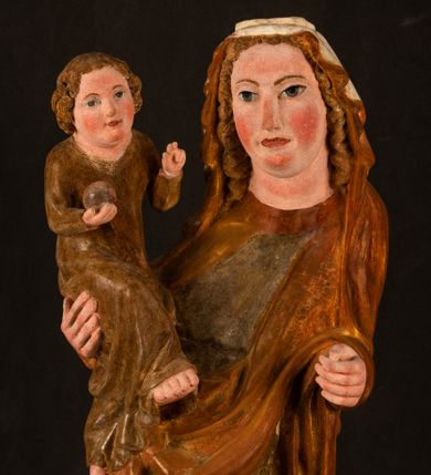 Zdjęcie nr 1: Rzeźba drążona, ustawiona na niewielkim, wielobocznym postumencie. Stojąca Maria ukazana frontalnie, w silnym kontrapoście z esowato wygiętym ciałem. Na lewej ręce podtrzymuje siedzące Dzieciątko, w prawej ręce ugiętej w łokciu i wyciągniętej do przodu najpewniej znajdowało się kiedyś berło.  Maria została ukazana jako młoda kobieta o owalnej twarzy, dużych, migdałowatych oczach, długim, prostym nosie i wyraźnie zaakcentowanych, dużych ustach. Karnacja jasna z rumieńcem zaznaczonym na policzkach i podbródku. Długie, jasne i falowane włosy częściowo zakryte chustą, symetrycznie okalają twarz postaci, spadając na jej ramiona. Maria jest ubrana w długą, sięgającą ziemi suknię, spod której widoczne są ostro zakończone czubki złotych butów oraz obszerny, złoty płaszcz tworzący ostro załamujące się fałdy na wysokości kolan Marii i formujący kaskadę wzdłuż prawego boku postaci. Na głowie Marii znajduje się biała chusta ze złota lamówką. Dzieciątko Jezus ukazane w pozycji siedzącej z lewą nogą wysuniętą wyraźnie do przodu. Prawą ręką wykonuje gest błogosławieństwa, w lewej trzyma niewielkie jabłko. Chłopiec o okrągłej, pulchnej twarzy i  krótkich, falowanych włosach spogląda przed siebie. Ubrany jest w wąską, suknię o długich rękawach, wykończoną przy dekolcie złotą lamówką. Spod sukni widoczne są bose stopy postaci. Karnacje postaci i część szat polichromowane, suknia Marii srebrzona, płaszcz i buty złocone.