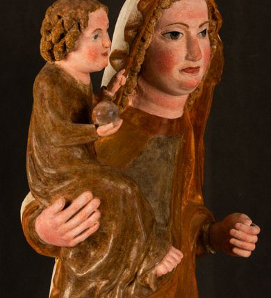 Zdjęcie nr 3: Rzeźba drążona, ustawiona na niewielkim, wielobocznym postumencie. Stojąca Maria ukazana frontalnie, w silnym kontrapoście z esowato wygiętym ciałem. Na lewej ręce podtrzymuje siedzące Dzieciątko, w prawej ręce ugiętej w łokciu i wyciągniętej do przodu najpewniej znajdowało się kiedyś berło.  Maria została ukazana jako młoda kobieta o owalnej twarzy, dużych, migdałowatych oczach, długim, prostym nosie i wyraźnie zaakcentowanych, dużych ustach. Karnacja jasna z rumieńcem zaznaczonym na policzkach i podbródku. Długie, jasne i falowane włosy częściowo zakryte chustą, symetrycznie okalają twarz postaci, spadając na jej ramiona. Maria jest ubrana w długą, sięgającą ziemi suknię, spod której widoczne są ostro zakończone czubki złotych butów oraz obszerny, złoty płaszcz tworzący ostro załamujące się fałdy na wysokości kolan Marii i formujący kaskadę wzdłuż prawego boku postaci. Na głowie Marii znajduje się biała chusta ze złota lamówką. Dzieciątko Jezus ukazane w pozycji siedzącej z lewą nogą wysuniętą wyraźnie do przodu. Prawą ręką wykonuje gest błogosławieństwa, w lewej trzyma niewielkie jabłko. Chłopiec o okrągłej, pulchnej twarzy i  krótkich, falowanych włosach spogląda przed siebie. Ubrany jest w wąską, suknię o długich rękawach, wykończoną przy dekolcie złotą lamówką. Spod sukni widoczne są bose stopy postaci. Karnacje postaci i część szat polichromowane, suknia Marii srebrzona, płaszcz i buty złocone.