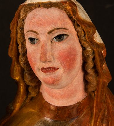 Zdjęcie nr 12: Rzeźba drążona, ustawiona na niewielkim, wielobocznym postumencie. Stojąca Maria ukazana frontalnie, w silnym kontrapoście z esowato wygiętym ciałem. Na lewej ręce podtrzymuje siedzące Dzieciątko, w prawej ręce ugiętej w łokciu i wyciągniętej do przodu najpewniej znajdowało się kiedyś berło.  Maria została ukazana jako młoda kobieta o owalnej twarzy, dużych, migdałowatych oczach, długim, prostym nosie i wyraźnie zaakcentowanych, dużych ustach. Karnacja jasna z rumieńcem zaznaczonym na policzkach i podbródku. Długie, jasne i falowane włosy częściowo zakryte chustą, symetrycznie okalają twarz postaci, spadając na jej ramiona. Maria jest ubrana w długą, sięgającą ziemi suknię, spod której widoczne są ostro zakończone czubki złotych butów oraz obszerny, złoty płaszcz tworzący ostro załamujące się fałdy na wysokości kolan Marii i formujący kaskadę wzdłuż prawego boku postaci. Na głowie Marii znajduje się biała chusta ze złota lamówką. Dzieciątko Jezus ukazane w pozycji siedzącej z lewą nogą wysuniętą wyraźnie do przodu. Prawą ręką wykonuje gest błogosławieństwa, w lewej trzyma niewielkie jabłko. Chłopiec o okrągłej, pulchnej twarzy i  krótkich, falowanych włosach spogląda przed siebie. Ubrany jest w wąską, suknię o długich rękawach, wykończoną przy dekolcie złotą lamówką. Spod sukni widoczne są bose stopy postaci. Karnacje postaci i część szat polichromowane, suknia Marii srebrzona, płaszcz i buty złocone.