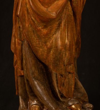 Zdjęcie nr 6: Rzeźba drążona, ustawiona na niewielkim, wielobocznym postumencie. Stojąca Maria ukazana frontalnie, w silnym kontrapoście z esowato wygiętym ciałem. Na lewej ręce podtrzymuje siedzące Dzieciątko, w prawej ręce ugiętej w łokciu i wyciągniętej do przodu najpewniej znajdowało się kiedyś berło.  Maria została ukazana jako młoda kobieta o owalnej twarzy, dużych, migdałowatych oczach, długim, prostym nosie i wyraźnie zaakcentowanych, dużych ustach. Karnacja jasna z rumieńcem zaznaczonym na policzkach i podbródku. Długie, jasne i falowane włosy częściowo zakryte chustą, symetrycznie okalają twarz postaci, spadając na jej ramiona. Maria jest ubrana w długą, sięgającą ziemi suknię, spod której widoczne są ostro zakończone czubki złotych butów oraz obszerny, złoty płaszcz tworzący ostro załamujące się fałdy na wysokości kolan Marii i formujący kaskadę wzdłuż prawego boku postaci. Na głowie Marii znajduje się biała chusta ze złota lamówką. Dzieciątko Jezus ukazane w pozycji siedzącej z lewą nogą wysuniętą wyraźnie do przodu. Prawą ręką wykonuje gest błogosławieństwa, w lewej trzyma niewielkie jabłko. Chłopiec o okrągłej, pulchnej twarzy i  krótkich, falowanych włosach spogląda przed siebie. Ubrany jest w wąską, suknię o długich rękawach, wykończoną przy dekolcie złotą lamówką. Spod sukni widoczne są bose stopy postaci. Karnacje postaci i część szat polichromowane, suknia Marii srebrzona, płaszcz i buty złocone.