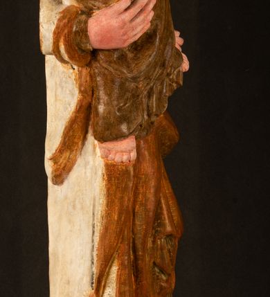 Zdjęcie nr 19: Rzeźba drążona, ustawiona na niewielkim, wielobocznym postumencie. Stojąca Maria ukazana frontalnie, w silnym kontrapoście z esowato wygiętym ciałem. Na lewej ręce podtrzymuje siedzące Dzieciątko, w prawej ręce ugiętej w łokciu i wyciągniętej do przodu najpewniej znajdowało się kiedyś berło.  Maria została ukazana jako młoda kobieta o owalnej twarzy, dużych, migdałowatych oczach, długim, prostym nosie i wyraźnie zaakcentowanych, dużych ustach. Karnacja jasna z rumieńcem zaznaczonym na policzkach i podbródku. Długie, jasne i falowane włosy częściowo zakryte chustą, symetrycznie okalają twarz postaci, spadając na jej ramiona. Maria jest ubrana w długą, sięgającą ziemi suknię, spod której widoczne są ostro zakończone czubki złotych butów oraz obszerny, złoty płaszcz tworzący ostro załamujące się fałdy na wysokości kolan Marii i formujący kaskadę wzdłuż prawego boku postaci. Na głowie Marii znajduje się biała chusta ze złota lamówką. Dzieciątko Jezus ukazane w pozycji siedzącej z lewą nogą wysuniętą wyraźnie do przodu. Prawą ręką wykonuje gest błogosławieństwa, w lewej trzyma niewielkie jabłko. Chłopiec o okrągłej, pulchnej twarzy i  krótkich, falowanych włosach spogląda przed siebie. Ubrany jest w wąską, suknię o długich rękawach, wykończoną przy dekolcie złotą lamówką. Spod sukni widoczne są bose stopy postaci. Karnacje postaci i część szat polichromowane, suknia Marii srebrzona, płaszcz i buty złocone.