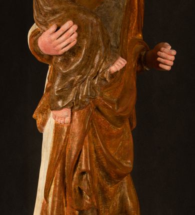 Zdjęcie nr 18: Rzeźba drążona, ustawiona na niewielkim, wielobocznym postumencie. Stojąca Maria ukazana frontalnie, w silnym kontrapoście z esowato wygiętym ciałem. Na lewej ręce podtrzymuje siedzące Dzieciątko, w prawej ręce ugiętej w łokciu i wyciągniętej do przodu najpewniej znajdowało się kiedyś berło.  Maria została ukazana jako młoda kobieta o owalnej twarzy, dużych, migdałowatych oczach, długim, prostym nosie i wyraźnie zaakcentowanych, dużych ustach. Karnacja jasna z rumieńcem zaznaczonym na policzkach i podbródku. Długie, jasne i falowane włosy częściowo zakryte chustą, symetrycznie okalają twarz postaci, spadając na jej ramiona. Maria jest ubrana w długą, sięgającą ziemi suknię, spod której widoczne są ostro zakończone czubki złotych butów oraz obszerny, złoty płaszcz tworzący ostro załamujące się fałdy na wysokości kolan Marii i formujący kaskadę wzdłuż prawego boku postaci. Na głowie Marii znajduje się biała chusta ze złota lamówką. Dzieciątko Jezus ukazane w pozycji siedzącej z lewą nogą wysuniętą wyraźnie do przodu. Prawą ręką wykonuje gest błogosławieństwa, w lewej trzyma niewielkie jabłko. Chłopiec o okrągłej, pulchnej twarzy i  krótkich, falowanych włosach spogląda przed siebie. Ubrany jest w wąską, suknię o długich rękawach, wykończoną przy dekolcie złotą lamówką. Spod sukni widoczne są bose stopy postaci. Karnacje postaci i część szat polichromowane, suknia Marii srebrzona, płaszcz i buty złocone.