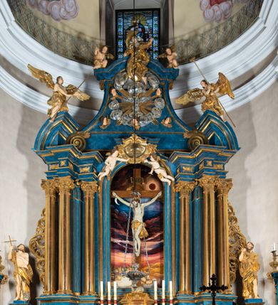 Zdjęcie nr 16: Ołtarz architektoniczny, jednoosiowy, jednokondygnacyjny ze zwieńczeniem. Na zdwojonych cokołach usytuowanych ukośnie względem osi po trzy kompozytowe kolumny opinające filary o gładkich trzonach podtrzymujących wyłamujące się nad nimi belkowanie z ćwierćkolistymi naczółkami. Na nich siedzące anioły z narzędzami męki Pańskiej. Pośrodku wnęka zamknięta półkoliście i wchodząca w partię belkowania z figurą Ukrzyżowanego. Nad wnęką dwa nagie putta trzymają kartusz z napisem: "DZIEŁO / NIE MAJĄC PRZYKŁADU / ŁASKA NIE ZASŁUŻONA / DAR NIE OCENIONY / MIŁOŚĆ BEZ GRANIC".  Zwieńczenie ujęte spływami wolutowymi, mocno zwężające się ku górze, zakończone gzymsem w formie łuku nadwieszonego. W polu owalny prześwit z glorią promienistą w chmurach z figurą Boga Ojca, puttami siedzącymi na gzymsie i główkami aniołów wśród chmur. Po bokach ołtarza dwie bramki z cokołami ujętymi spływami wolutowymi, na których figury św. Jana Chrzciciela i św. Jana Ewangelisty. Dekoracja ornamentalna w postaci rozłożystych liści na cokołach oraz liściastych, ażurowych uszy ujmujących nastawę. 