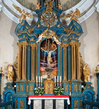 Zdjęcie nr 49: Ołtarz architektoniczny, jednoosiowy, jednokondygnacyjny ze zwieńczeniem. Na zdwojonych cokołach usytuowanych ukośnie względem osi po trzy kompozytowe kolumny opinające filary o gładkich trzonach podtrzymujących wyłamujące się nad nimi belkowanie z ćwierćkolistymi naczółkami. Na nich siedzące anioły z narzędzami męki Pańskiej. Pośrodku wnęka zamknięta półkoliście i wchodząca w partię belkowania z figurą Ukrzyżowanego. Nad wnęką dwa nagie putta trzymają kartusz z napisem: &quot;DZIEŁO / NIE MAJĄC PRZYKŁADU / ŁASKA NIE ZASŁUŻONA / DAR NIE OCENIONY / MIŁOŚĆ BEZ GRANIC&quot;.  Zwieńczenie ujęte spływami wolutowymi, mocno zwężające się ku górze, zakończone gzymsem w formie łuku nadwieszonego. W polu owalny prześwit z glorią promienistą w chmurach z figurą Boga Ojca, puttami siedzącymi na gzymsie i główkami aniołów wśród chmur. Po bokach ołtarza dwie bramki z cokołami ujętymi spływami wolutowymi, na których figury św. Jana Chrzciciela i św. Jana Ewangelisty. Dekoracja ornamentalna w postaci rozłożystych liści na cokołach oraz liściastych, ażurowych uszy ujmujących nastawę. 