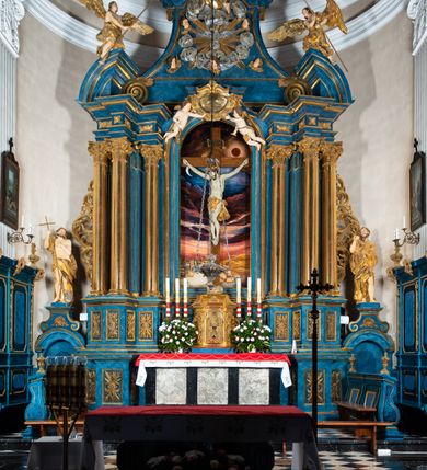 Zdjęcie nr 1: Ołtarz architektoniczny, jednoosiowy, jednokondygnacyjny ze zwieńczeniem. Na zdwojonych cokołach usytuowanych ukośnie względem osi po trzy kompozytowe kolumny opinające filary o gładkich trzonach podtrzymujących wyłamujące się nad nimi belkowanie z ćwierćkolistymi naczółkami. Na nich siedzące anioły z narzędzami męki Pańskiej. Pośrodku wnęka zamknięta półkoliście i wchodząca w partię belkowania z figurą Ukrzyżowanego. Nad wnęką dwa nagie putta trzymają kartusz z napisem: &quot;DZIEŁO / NIE MAJĄC PRZYKŁADU / ŁASKA NIE ZASŁUŻONA / DAR NIE OCENIONY / MIŁOŚĆ BEZ GRANIC&quot;.  Zwieńczenie ujęte spływami wolutowymi, mocno zwężające się ku górze, zakończone gzymsem w formie łuku nadwieszonego. W polu owalny prześwit z glorią promienistą w chmurach z figurą Boga Ojca, puttami siedzącymi na gzymsie i główkami aniołów wśród chmur. Po bokach ołtarza dwie bramki z cokołami ujętymi spływami wolutowymi, na których figury św. Jana Chrzciciela i św. Jana Ewangelisty. Dekoracja ornamentalna w postaci rozłożystych liści na cokołach oraz liściastych, ażurowych uszy ujmujących nastawę. 