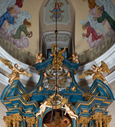 Zdjęcie nr 11: Ołtarz architektoniczny, jednoosiowy, jednokondygnacyjny ze zwieńczeniem. Na zdwojonych cokołach usytuowanych ukośnie względem osi po trzy kompozytowe kolumny opinające filary o gładkich trzonach podtrzymujących wyłamujące się nad nimi belkowanie z ćwierćkolistymi naczółkami. Na nich siedzące anioły z narzędzami męki Pańskiej. Pośrodku wnęka zamknięta półkoliście i wchodząca w partię belkowania z figurą Ukrzyżowanego. Nad wnęką dwa nagie putta trzymają kartusz z napisem: &quot;DZIEŁO / NIE MAJĄC PRZYKŁADU / ŁASKA NIE ZASŁUŻONA / DAR NIE OCENIONY / MIŁOŚĆ BEZ GRANIC&quot;.  Zwieńczenie ujęte spływami wolutowymi, mocno zwężające się ku górze, zakończone gzymsem w formie łuku nadwieszonego. W polu owalny prześwit z glorią promienistą w chmurach z figurą Boga Ojca, puttami siedzącymi na gzymsie i główkami aniołów wśród chmur. Po bokach ołtarza dwie bramki z cokołami ujętymi spływami wolutowymi, na których figury św. Jana Chrzciciela i św. Jana Ewangelisty. Dekoracja ornamentalna w postaci rozłożystych liści na cokołach oraz liściastych, ażurowych uszy ujmujących nastawę. 