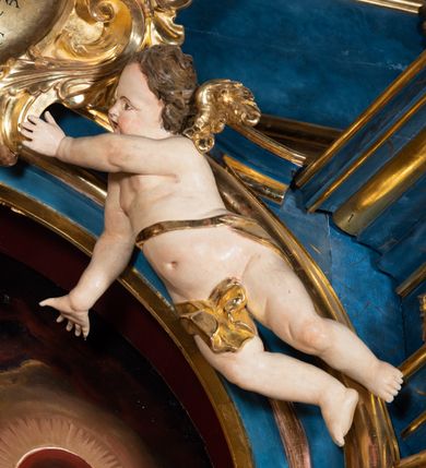 Zdjęcie nr 14: Ołtarz architektoniczny, jednoosiowy, jednokondygnacyjny ze zwieńczeniem. Na zdwojonych cokołach usytuowanych ukośnie względem osi po trzy kompozytowe kolumny opinające filary o gładkich trzonach podtrzymujących wyłamujące się nad nimi belkowanie z ćwierćkolistymi naczółkami. Na nich siedzące anioły z narzędzami męki Pańskiej. Pośrodku wnęka zamknięta półkoliście i wchodząca w partię belkowania z figurą Ukrzyżowanego. Nad wnęką dwa nagie putta trzymają kartusz z napisem: &quot;DZIEŁO / NIE MAJĄC PRZYKŁADU / ŁASKA NIE ZASŁUŻONA / DAR NIE OCENIONY / MIŁOŚĆ BEZ GRANIC&quot;.  Zwieńczenie ujęte spływami wolutowymi, mocno zwężające się ku górze, zakończone gzymsem w formie łuku nadwieszonego. W polu owalny prześwit z glorią promienistą w chmurach z figurą Boga Ojca, puttami siedzącymi na gzymsie i główkami aniołów wśród chmur. Po bokach ołtarza dwie bramki z cokołami ujętymi spływami wolutowymi, na których figury św. Jana Chrzciciela i św. Jana Ewangelisty. Dekoracja ornamentalna w postaci rozłożystych liści na cokołach oraz liściastych, ażurowych uszy ujmujących nastawę. 