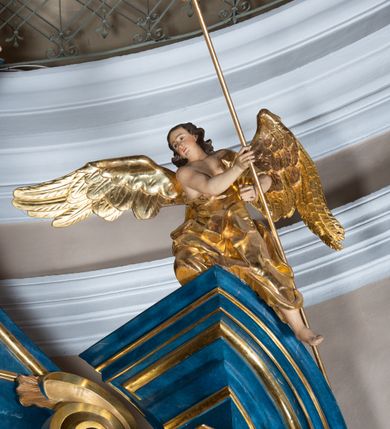 Zdjęcie nr 13: Ołtarz architektoniczny, jednoosiowy, jednokondygnacyjny ze zwieńczeniem. Na zdwojonych cokołach usytuowanych ukośnie względem osi po trzy kompozytowe kolumny opinające filary o gładkich trzonach podtrzymujących wyłamujące się nad nimi belkowanie z ćwierćkolistymi naczółkami. Na nich siedzące anioły z narzędzami męki Pańskiej. Pośrodku wnęka zamknięta półkoliście i wchodząca w partię belkowania z figurą Ukrzyżowanego. Nad wnęką dwa nagie putta trzymają kartusz z napisem: "DZIEŁO / NIE MAJĄC PRZYKŁADU / ŁASKA NIE ZASŁUŻONA / DAR NIE OCENIONY / MIŁOŚĆ BEZ GRANIC".  Zwieńczenie ujęte spływami wolutowymi, mocno zwężające się ku górze, zakończone gzymsem w formie łuku nadwieszonego. W polu owalny prześwit z glorią promienistą w chmurach z figurą Boga Ojca, puttami siedzącymi na gzymsie i główkami aniołów wśród chmur. Po bokach ołtarza dwie bramki z cokołami ujętymi spływami wolutowymi, na których figury św. Jana Chrzciciela i św. Jana Ewangelisty. Dekoracja ornamentalna w postaci rozłożystych liści na cokołach oraz liściastych, ażurowych uszy ujmujących nastawę. 